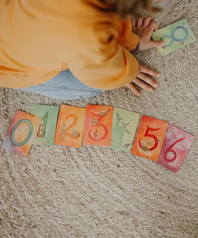 Child sorting the Grimms number cards from 0 to 6. Each card showing a corresponding number of illustrated animals