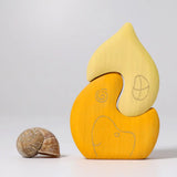 Grimm's yellow onion house stacking toy placed next to a snail shell. 2 piece wooden block set.