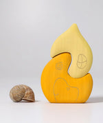 Grimm's yellow onion house stacking toy placed next to a snail shell. 2 piece wooden block set.