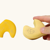 Close up of adult's hand holding a piece from the Grimm's yellow onion stacking toy.