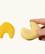 Close up of adult's hand holding a piece from the Grimm's yellow onion stacking toy.