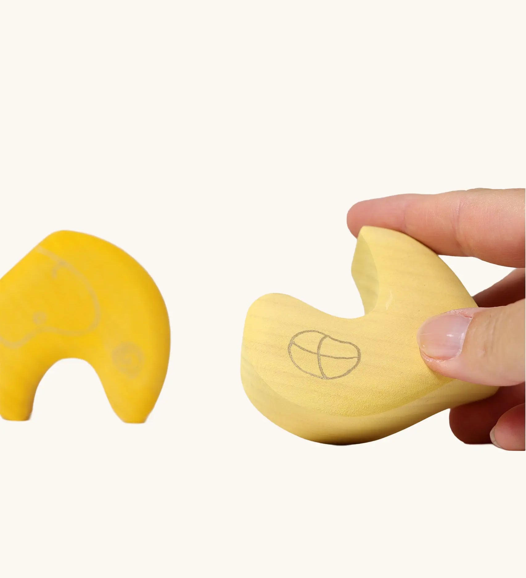 Close up of adult's hand holding a piece from the Grimm's yellow onion stacking toy.