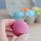 Adult hand holding a Grimms pastel wooden ball showing size