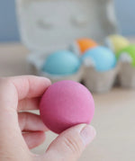 Adult hand holding a Grimms pastel wooden ball showing size