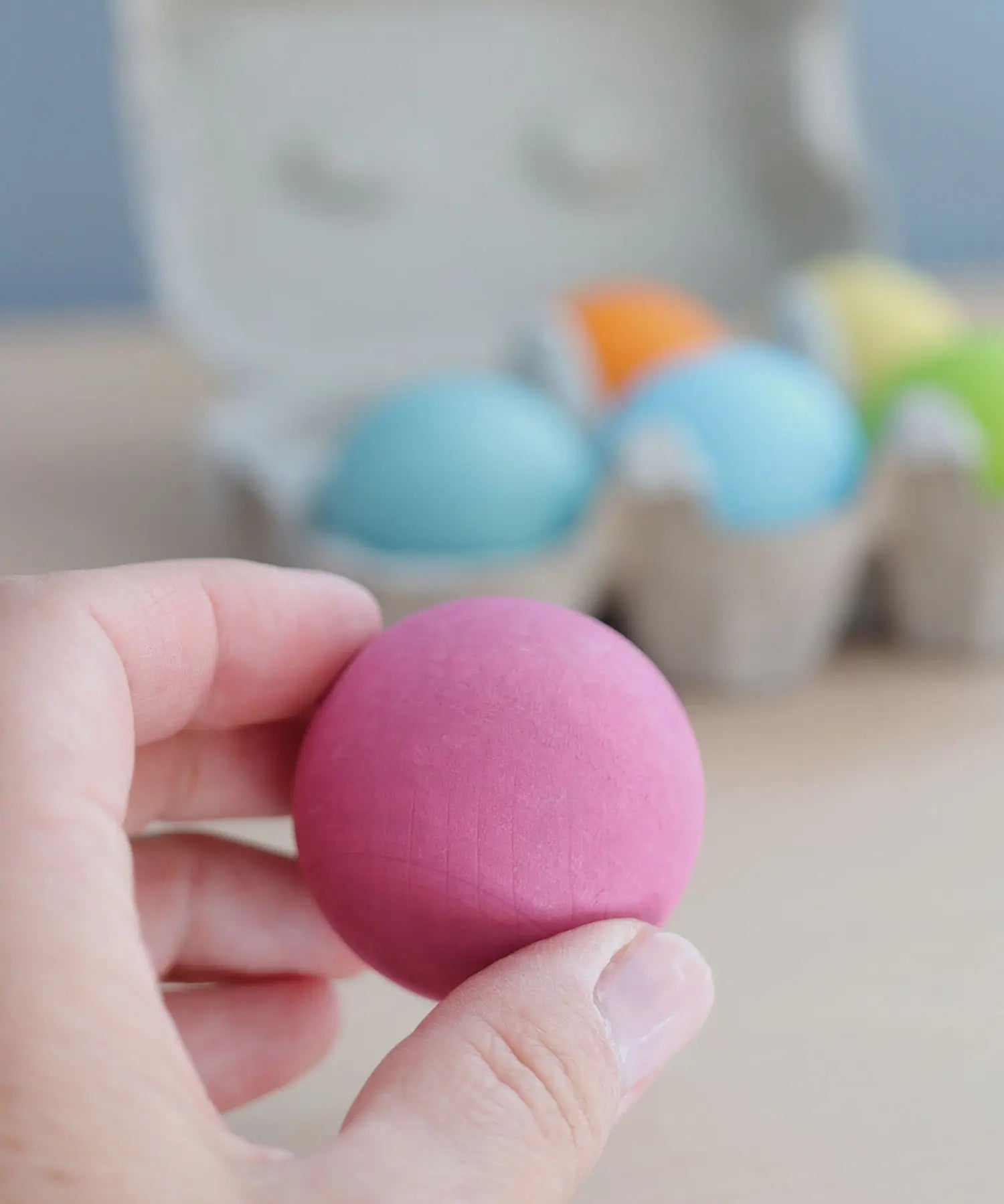 Adult hand holding a Grimms pastel wooden ball showing size