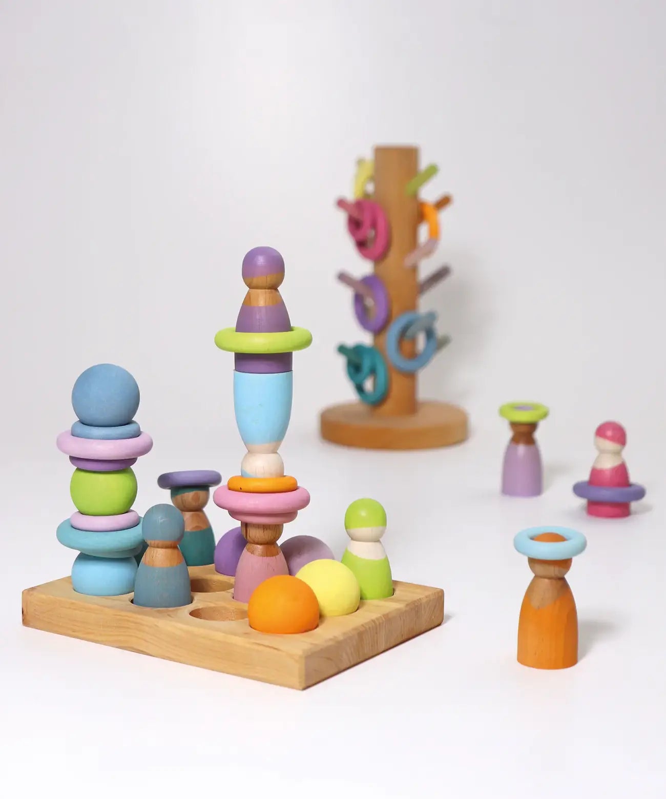 A pastel coloured play setup using Grimms small rainbow balls, rings, sorting board peg dolls