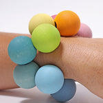 The Grimm's pastel grasper beads wooden grasping toy placed on an adult's wrist.