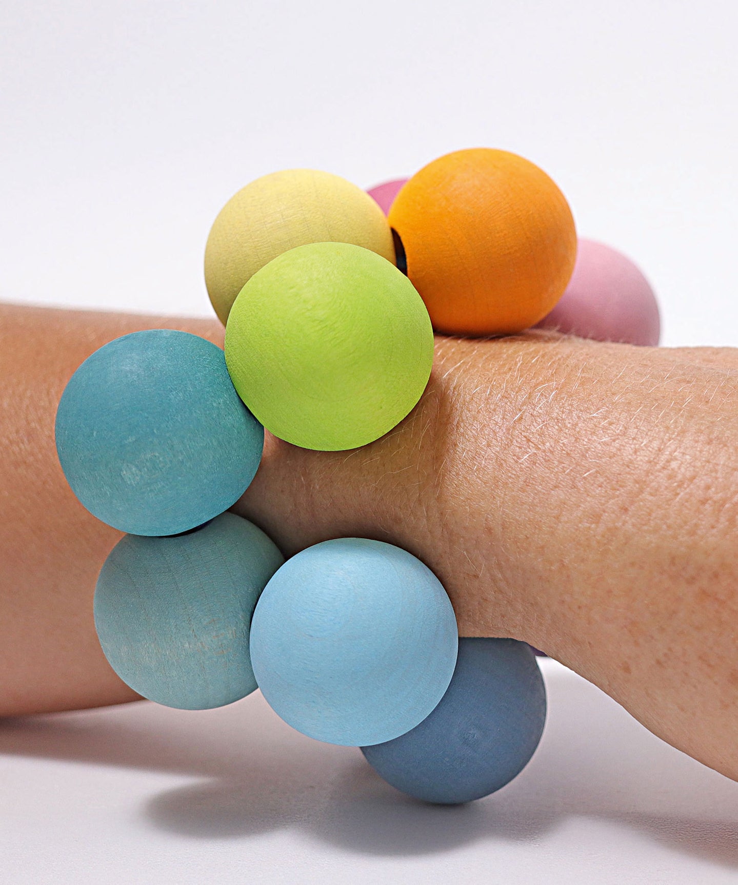 The Grimm's pastel grasper beads wooden grasping toy placed on an adult's wrist.