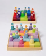 A rainbow and pastel Grimms 36 cube set in their wooden frames with peg dolls on top