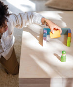 Child holding a wooden block next to a structure made from the Grimms pastel duo wooden block set