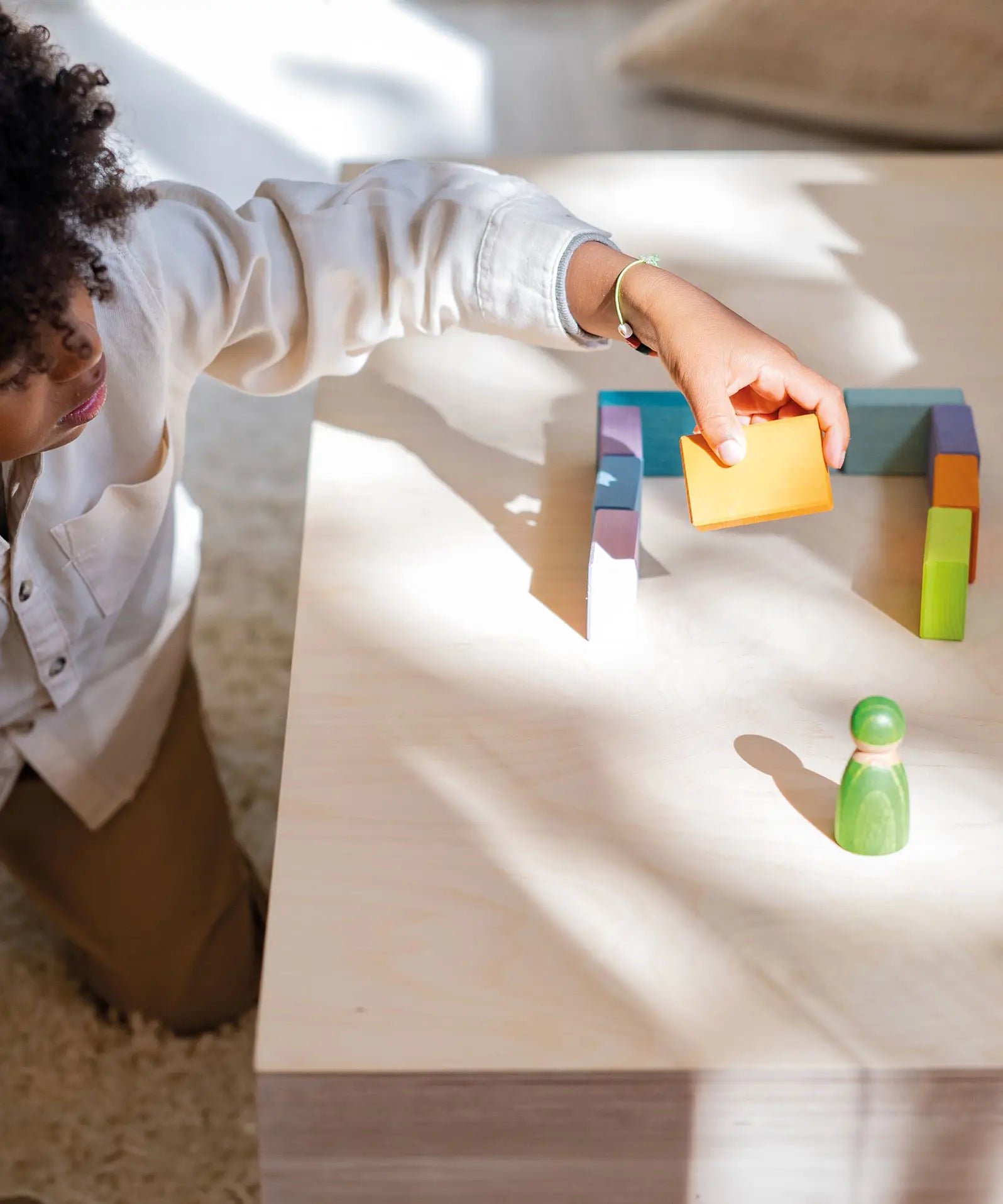 Child holding a wooden block next to a structure made from the Grimms pastel duo wooden block set