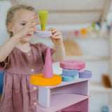 Child holding a light pink wooden disk with a loose Grimms forest piece on top 