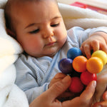 A baby holding a Grimm's Rainbow Beads Grasper.