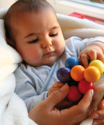 A baby holding a Grimm's Rainbow Beads Grasper.