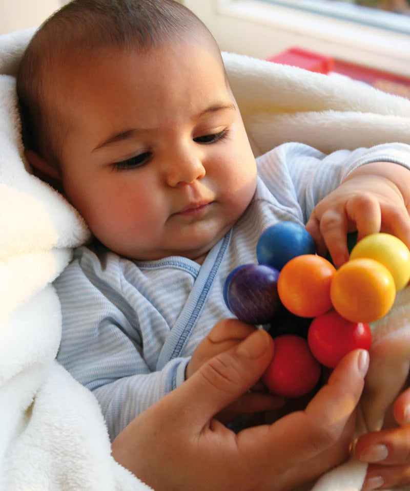 A baby holding a Grimm's Rainbow Beads Grasper.