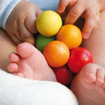 A close up of a baby holding the Grimm's Rainbow Beads Grasper toy.