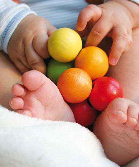 A close up of a baby holding the Grimm's Rainbow Beads Grasper toy.