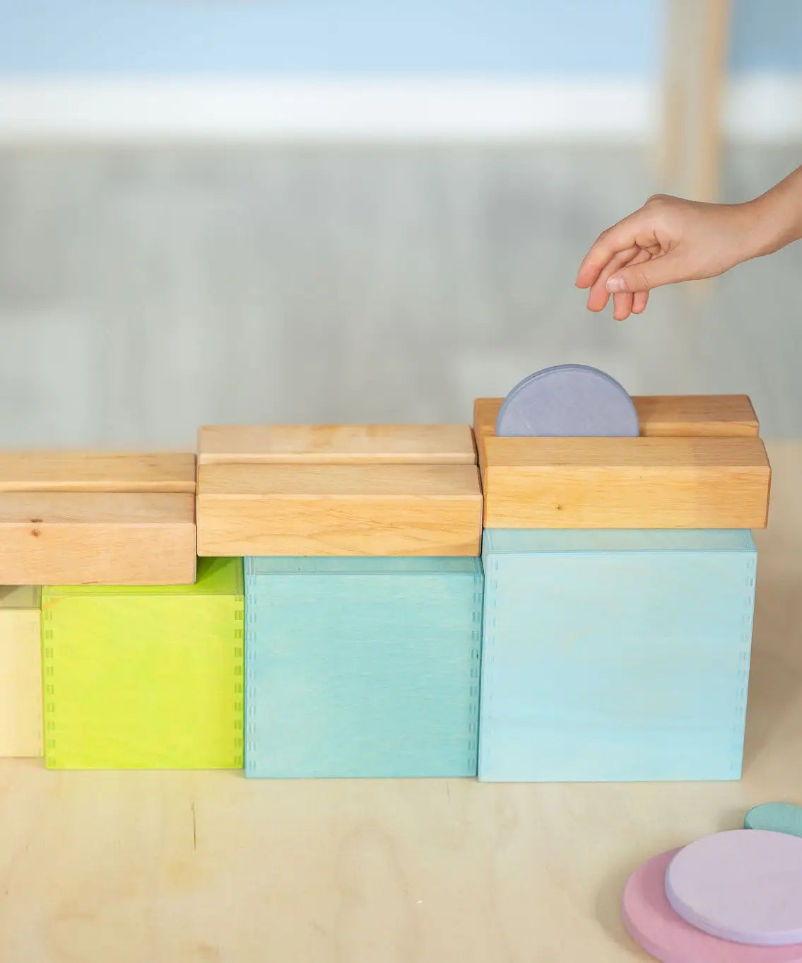 Child rolling a coin down a wooden rail on top of the Grimms large pastel building boxes