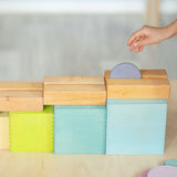 Child rolling a coin down a wooden rail on top of the Grimms large pastel building boxes