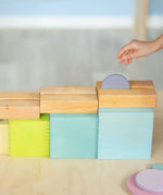 Child rolling a coin down a wooden rail on top of the Grimms large pastel building boxes