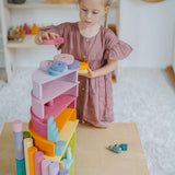 Child placing circular blocks on top of a stack made from Grimms pastel semi circles and arch pieces