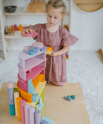 Child placing circular blocks on top of a stack made from Grimms pastel semi circles and arch pieces