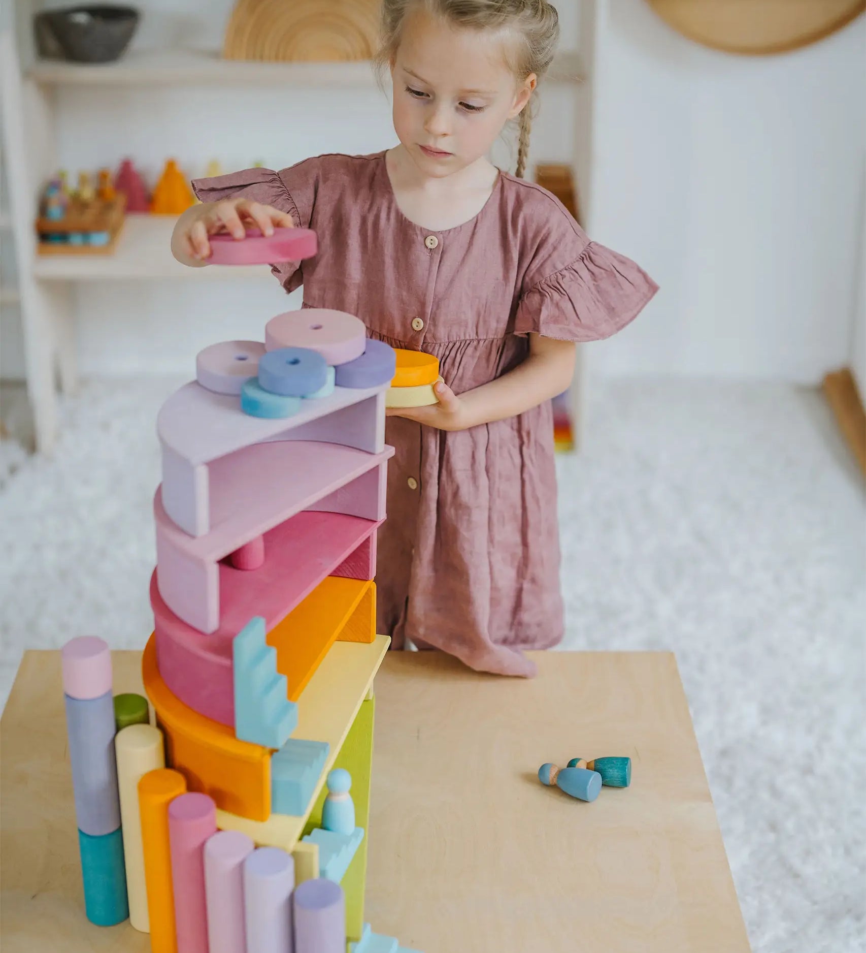 Child placing circular blocks on top of a stack made from Grimms pastel semi circles and arch pieces