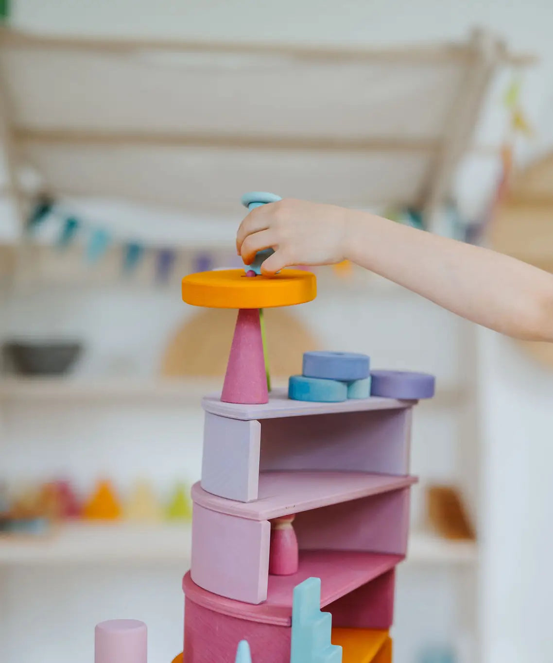 Child placing a block on top of a stack made from Grimms pastel semi circles and arch pieces
