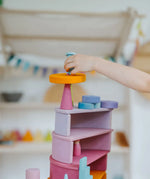 Child placing a block on top of a stack made from Grimms pastel semi circles and arch pieces
