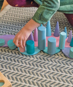 Child placing a pastel building block on a Grimms pastel semi circle piece