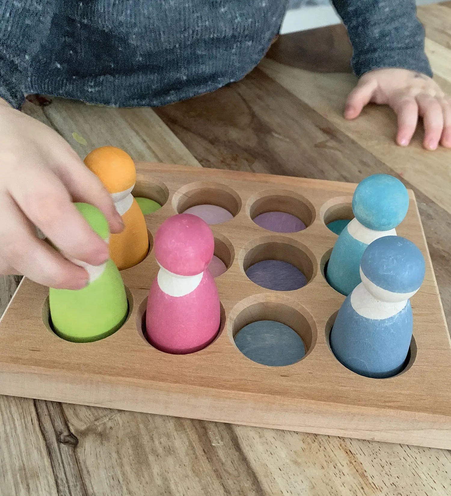 Child sorting pastel coloured wooden peg dolls in the Grimms handcrafted sorting board