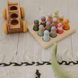 Grimms handcrafted sorting board with pastel coloured peg dolls sitting inside the round slots next to a toy bus 