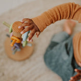 Top view of a child reaching out to a Grimms wooden sorting helper for rings in a pastel palette