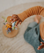 Top view of a child reaching out to a Grimms wooden sorting helper for rings in a pastel palette