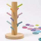 Grimms wooden sorting helper with pastel dowels and a round natural base with loose matching rings in the background
