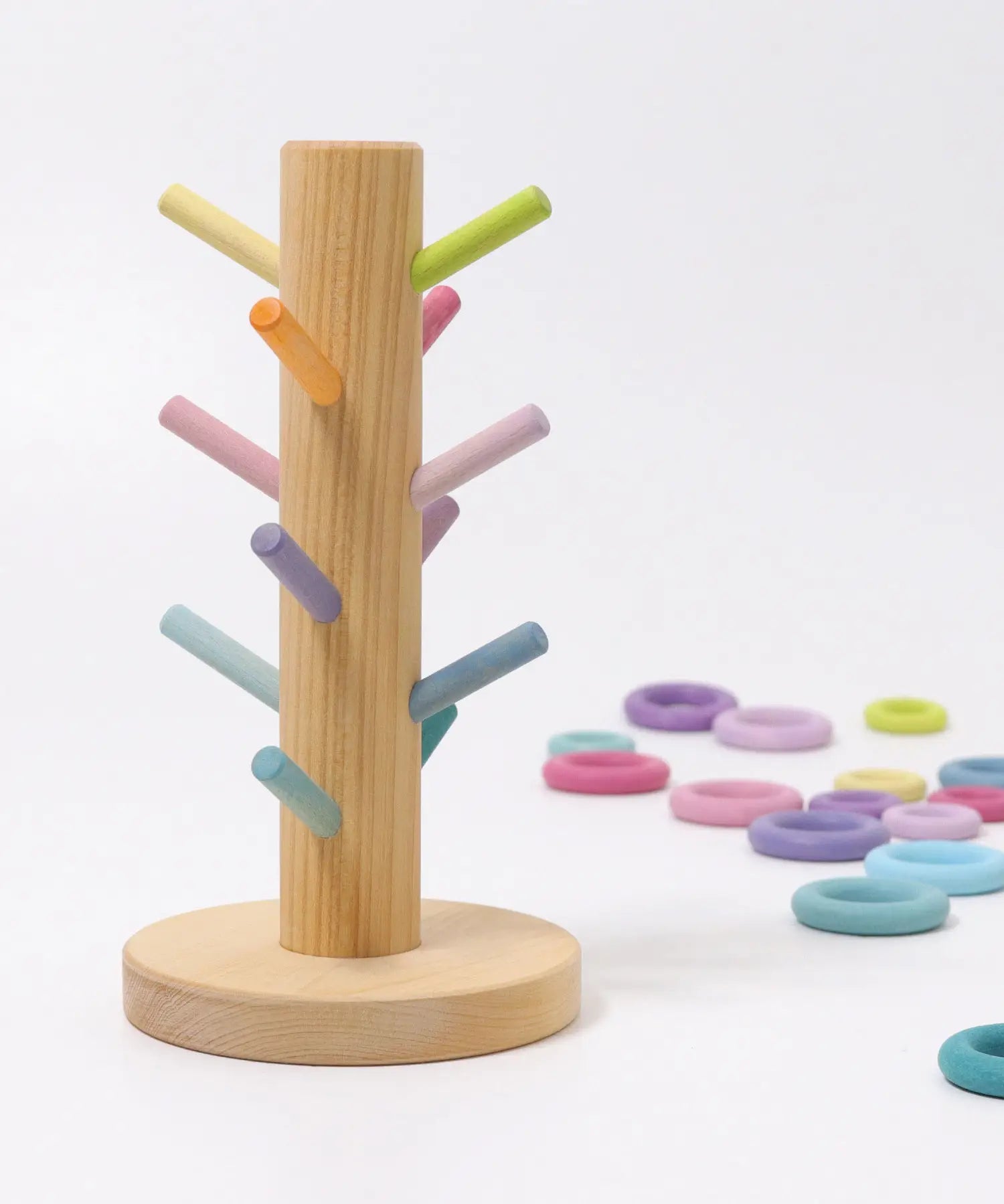 Grimms wooden sorting helper with pastel dowels and a round natural base with loose matching rings in the background
