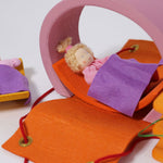 The Grimm's Pink Mobile Home wooden Toy Set set our with a doll laying in a bed on the orange arch piece.
