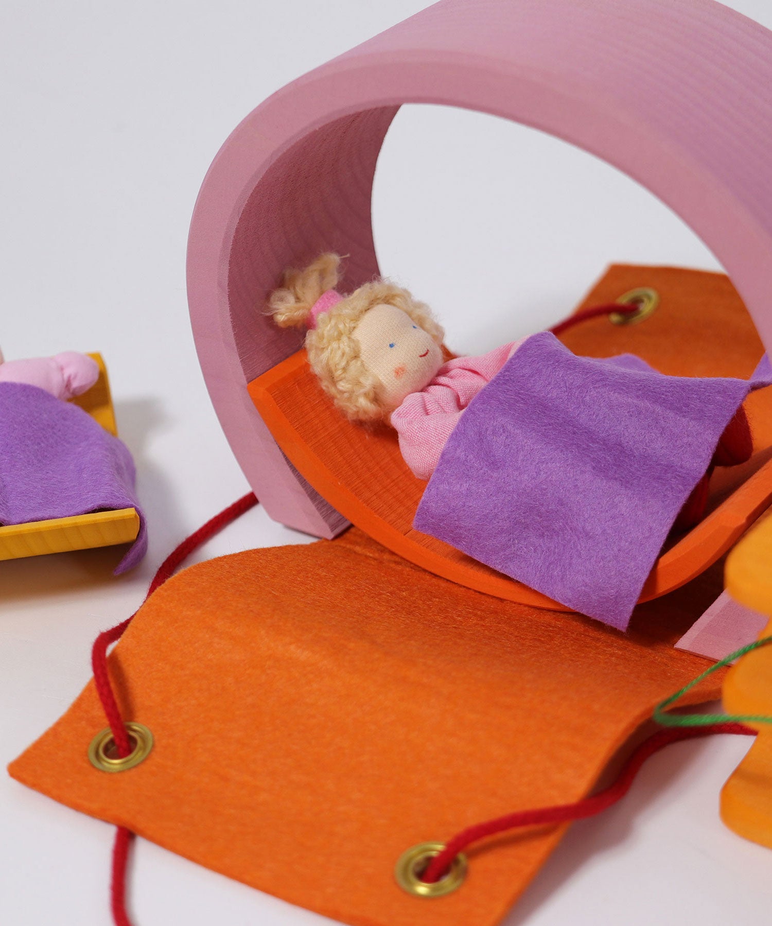 The Grimm's Pink Mobile Home wooden Toy Set set our with a doll laying in a bed on the orange arch piece.