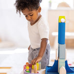 A child carefully balances a Grimms wooden figure on top of an arch