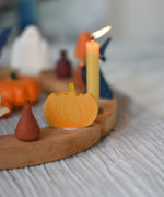 A Grimm's wooden decorative figure placed on a natural celebration ring. A lit beeswax candle and other figures can be seen in the background. The decorative figures are part of a wide range of Waldorf inspired figures and celebration rings available here at Babipur. 