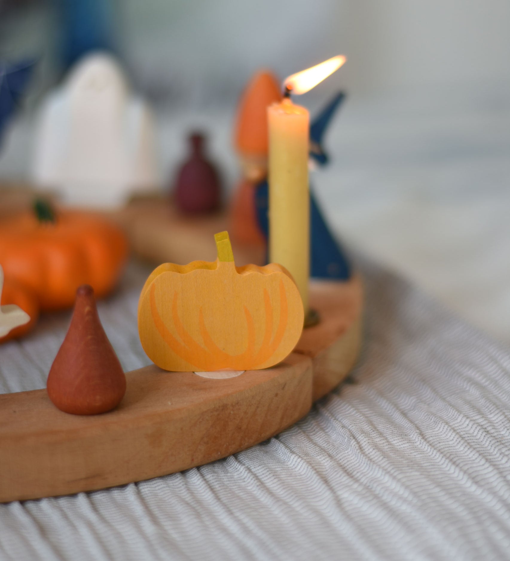 A Grimm's wooden decorative figure placed on a natural celebration ring. A lit beeswax candle and other figures can be seen in the background. The decorative figures are part of a wide range of Waldorf inspired figures and celebration rings available here at Babipur. 