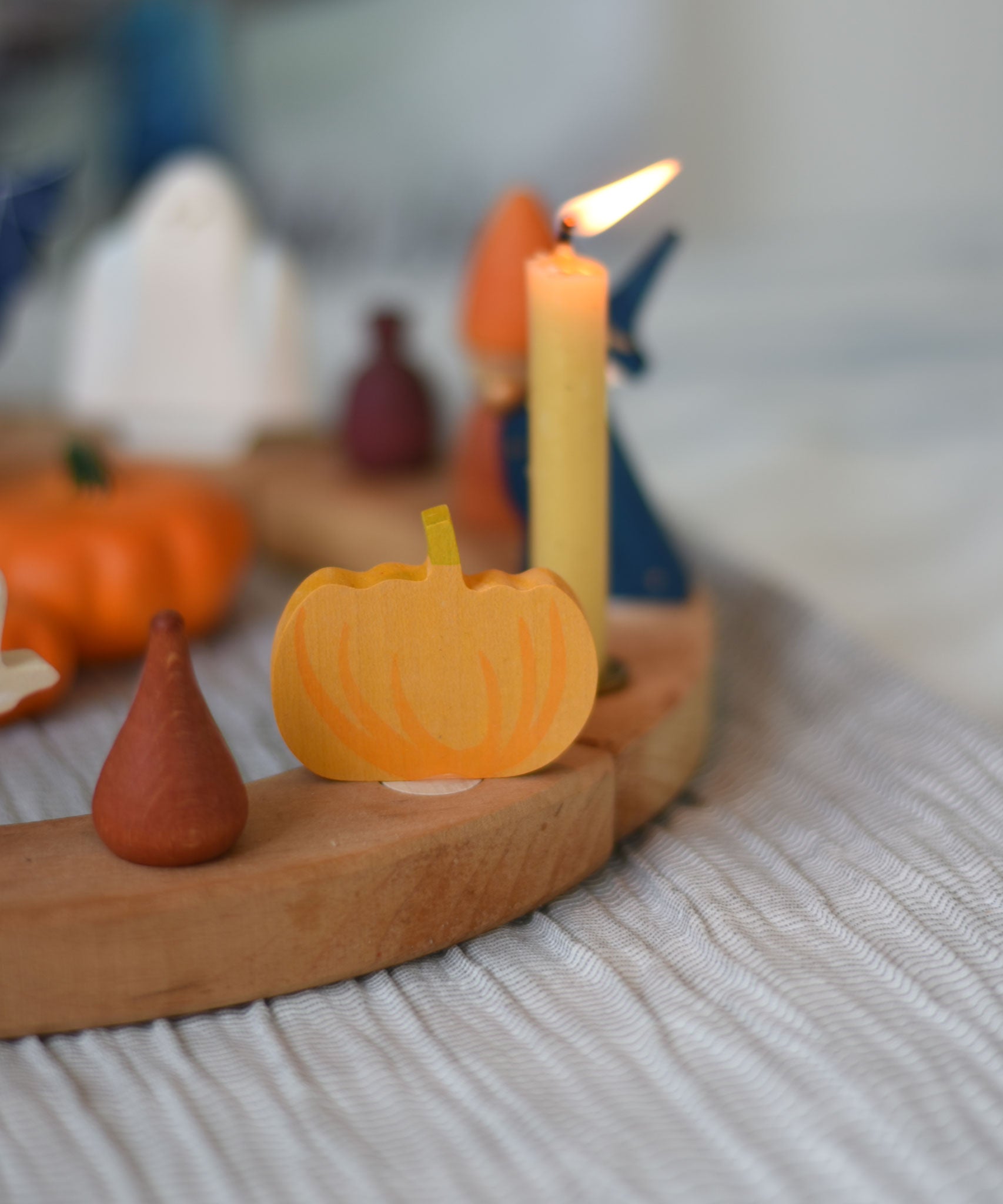 A Grimm's wooden decorative figure placed on a natural celebration ring. A lit beeswax candle and other figures can be seen in the background. The decorative figures are part of a wide range of Waldorf inspired figures and celebration rings available here at Babipur. 