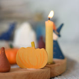 A close up of a Grimm's wooden decorative figure placed on a natural celebration ring. A lit beeswax candle and other figures can be seen in the background. The decorative figures are part of a wide range of Waldorf inspired figures and celebration rings available here at Babipur. 