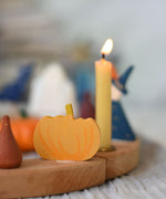 A close up of a Grimm's wooden decorative figure placed on a natural celebration ring. A lit beeswax candle and other figures can be seen in the background. The decorative figures are part of a wide range of Waldorf inspired figures and celebration rings available here at Babipur. 