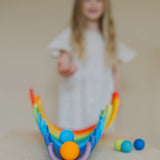 Child rolling a orange Grimms wooden ball down a line of arched building blocks