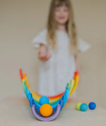 Child rolling a orange Grimms wooden ball down a line of arched building blocks