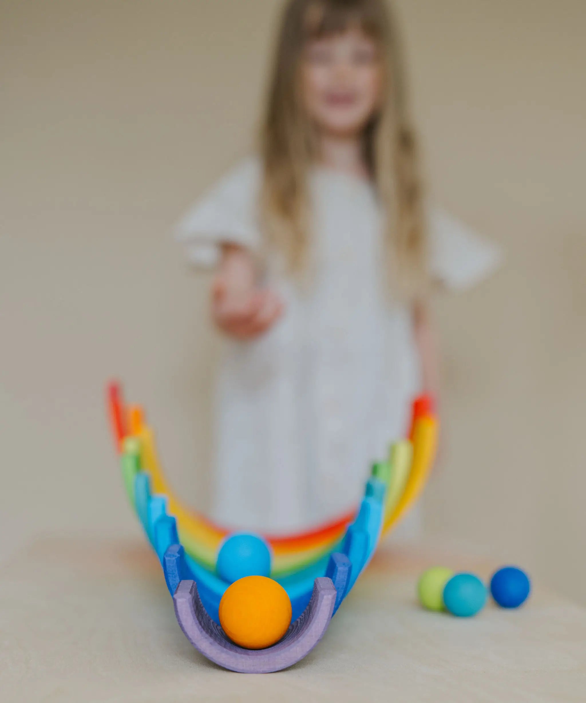 Child rolling a orange Grimms wooden ball down a line of arched building blocks