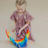 Child rolling a blue Grimms wooden ball down a line of arched building blocks