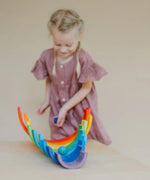 Child rolling a blue Grimms wooden ball down a line of arched building blocks