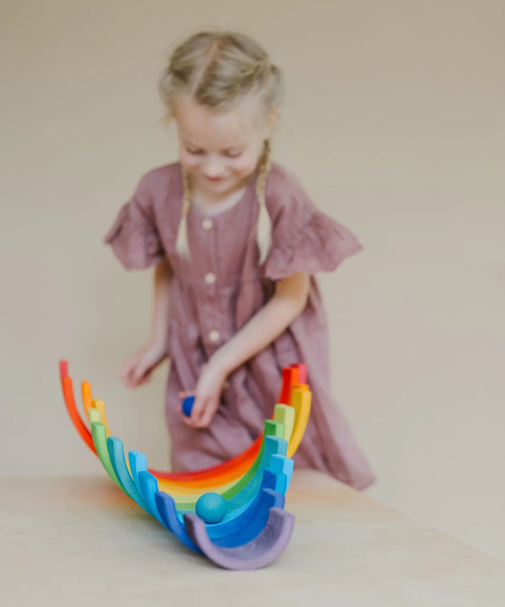Child rolling a blue Grimms wooden ball down a line of arched building blocks